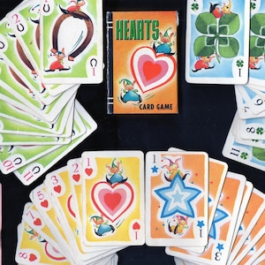 May include: Vintage Hearts card game with colorful illustrations. The game box and cards feature whimsical characters and symbols, including hearts, clovers, and stars. The cards are arranged in a fan shape, showcasing the game's design.