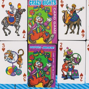 May include: A Crazy Eights card game set featuring illustrated playing cards with circus-themed characters and a clown. The card deck box is green with the game title and a clown illustration. The cards have numbers and suit symbols.