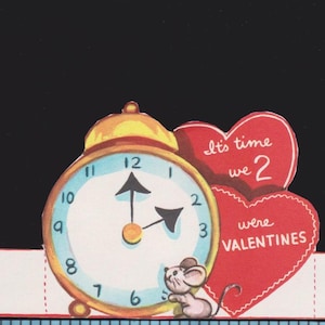 May include: A vintage-style paper Valentine card featuring a gold alarm clock and a small grey mouse. Two red hearts display the text It's time we 2 were VALENTINES. A blue measuring tape at the bottom shows the card is approximately 4 inches wide.