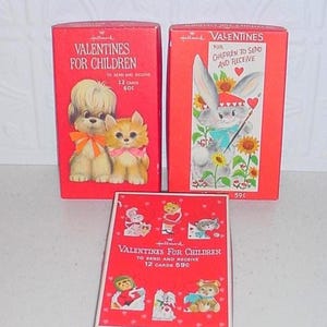 May include: Three red Hallmark boxes of Valentines for children. Two upright boxes feature illustrations of a puppy, kitten, and rabbit with sunflowers. The third box lies flat, displaying six small character cutouts and red heart patterns.
