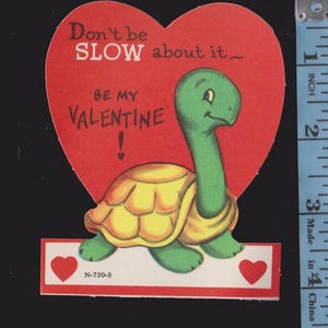 May include: Vintage Valentine's Day card featuring a green turtle with a yellow shell, set against a red heart background. The card reads "Don't be SLOW about it_ BE MY VALENTINE!" with two red hearts. The card is approximately 4 inches tall.