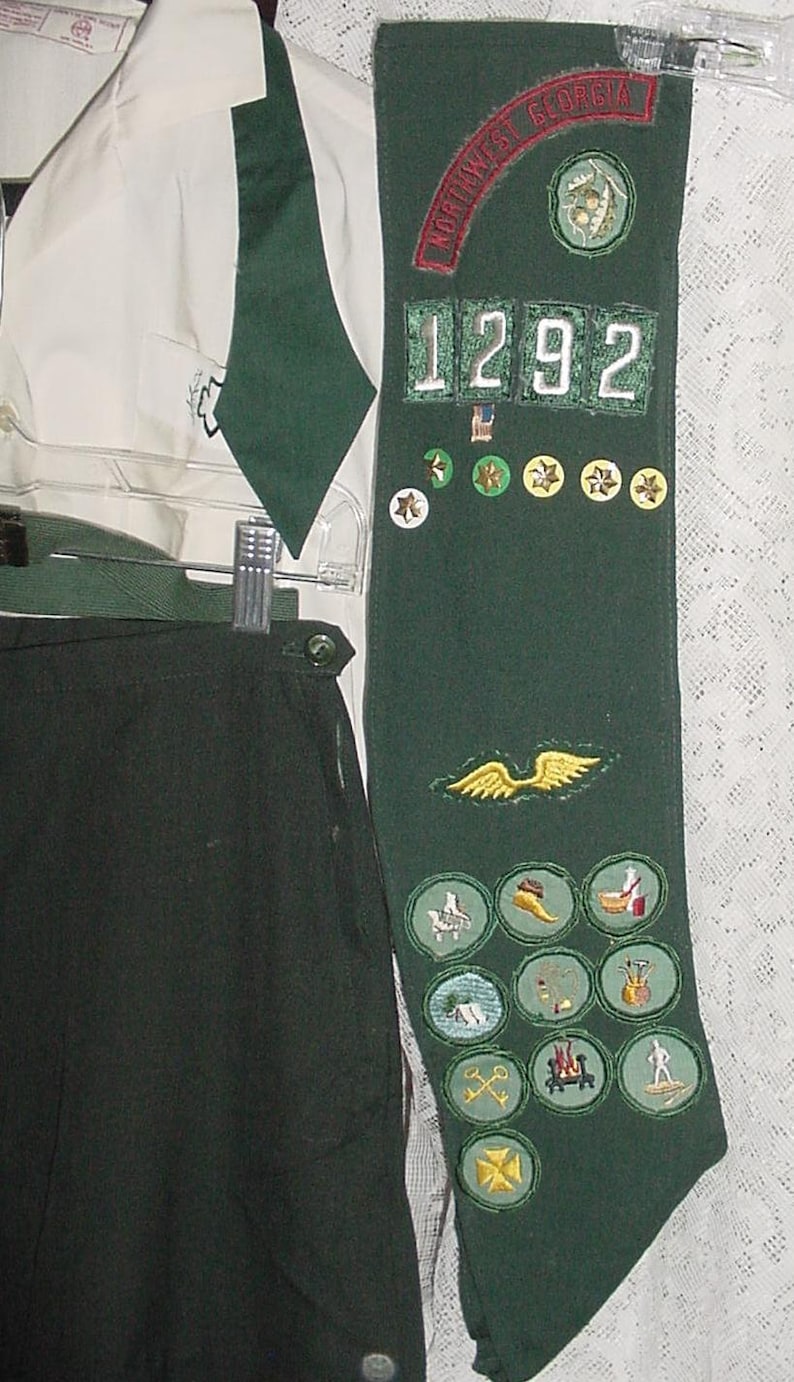 May include: A dark green sash with the text "NORTHWEST GEORGIA" and the number "1292" is displayed. The sash is adorned with various patches and badges, along with a white shirt and dark green pants.