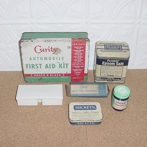 May include: An assortment of vintage medical supplies, including a Curity Automobile First Aid Kit, Epsom Salt tin, and a small jar of Vicks VapoRub. Other items include a white plastic container, a Curity Twist Type Tourniquet, and a tin of Sucrets.
