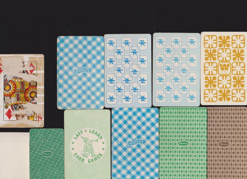 May include: A selection of vintage playing cards with diverse designs. The cards display patterns such as blue gingham, geometric shapes, and a green card with a cartoon character and the text "LAFF 'N LEARN CARD GAMES". Some cards show signs of wear.