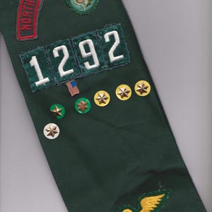 May include: A dark green sash with embroidered patches and pins. Patches include the text "NORTHWEST GEORGIA" in red, the number "1292" in white, and various emblems. Gold star pins and a small American flag pin are also visible.