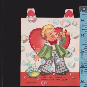May include: Vintage Valentine's Day card featuring a cartoon boy blowing heart-shaped bubbles. The boy wears a green jacket, plaid pants, and a red bow tie. The card has a red heart and the text "I GET ALL BUBBLY WHEN YOU ARE NEAR".