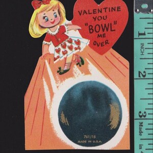 May include: Vintage Valentine's Day card featuring a cartoon girl in a red dress with heart accents, a red bow, and blonde hair. The card has a red heart with the text "VALENTINE YOU 'BOWL' ME OVER". A bowling ball is at the bottom. Made in the U.S.A.