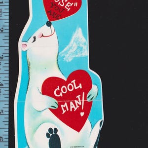 May include: A vintage-style die-cut paper valentine card featuring a white polar bear on a light blue background. The bear holds a red heart reading "COOL MAN" and a smaller red heart above its nose reading "I NOSE YOU ARE". A ruler shows it is 7 inches tall.