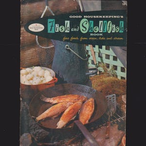 May include: Vintage cookbook cover titled "Good Housekeeping's Fish and Shellfish Book." The cover features a retro design with the title in teal and white. The image shows cooked fish in a pan, a pot of potatoes, and outdoor cooking elements.