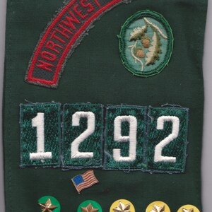 May include: Dark green fabric with embroidered patches and pins. Patches include "NORTHWEST GEORGIA" in red, a circular design, and the number "1292". Several star-shaped pins in gold and white are also present.