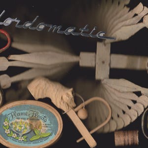 May include: A collection of vintage items including a silver-toned Fordomatic script emblem, a wooden fan-shaped tool, a rusty iron key, a carved wooden animal figure, a brass drawer pull, and an oval box labeled Flame Floats with candle art.