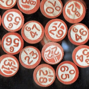 May include: A collection of vintage wooden bingo chips. Each chip features a white center with a red border and a number printed in red. The numbers vary, including 65, 28, 31, 56, 59, 47, 70, 29, 46, and 22.