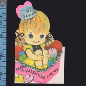 May include: Vintage Valentine's Day card featuring a cartoon girl with blonde hair and blue eyes. She wears a yellow dress and a hat that says "Hi Sugar." The card reads "Here's a Valentine for You" and includes a heart and cupcake.