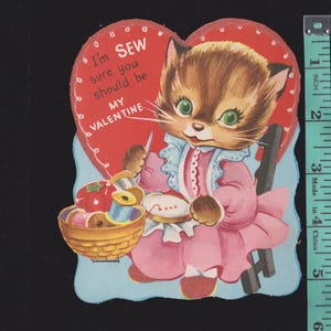 May include: Vintage Valentine's Day card featuring a cartoon cat in a pink dress, sewing. The card is heart-shaped with the text "I'm SEW sure you should be MY VALENTINE." A basket of sewing supplies is also shown.