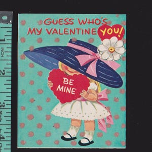 May include: Vintage Valentine's Day card featuring a girl in a large blue hat with a pink bow, holding a red heart that says "BE MINE." The card has a turquoise background with pink polka dots and the text "GUESS WHO'S MY VALENTINE YOU!"