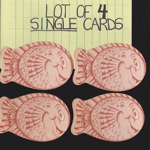 May include: Four pink fish-shaped cards with smiling faces and detailed fins. The cards are arranged in a square, with the text "LOT OF 4 SINGLE CARDS" on a yellow background in the upper portion of the image.