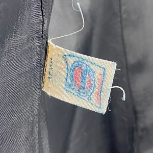 May include: A close-up of a white fabric label with blue and red stitching. The label has a blue circle with a white center and the text "Made in USA" printed on it.