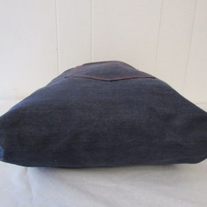 K&ouml;nnte beinhalten: Eine dunkelblaue Canvas-Tragetasche mit einer braunen Tasche auf der Vorderseite.