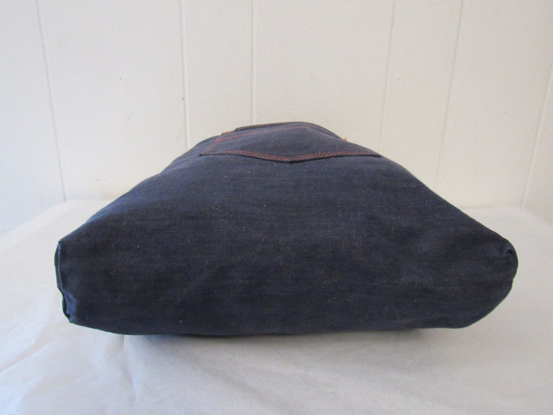 K&ouml;nnte beinhalten: Eine dunkelblaue Canvas-Tragetasche mit einer braunen Tasche auf der Vorderseite.