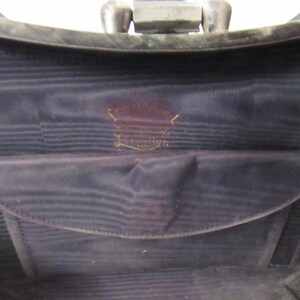 May include: The inside of a black purse with a black fabric lining and a small pocket. The purse has a gold label that reads "Genuine Leather."