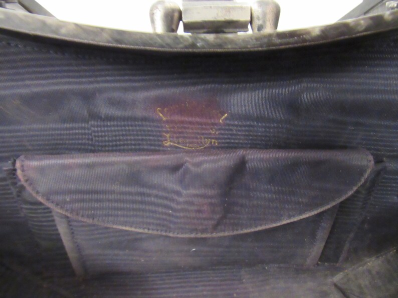 May include: The inside of a black purse with a black fabric lining and a small pocket. The purse has a gold label that reads "Genuine Leather."