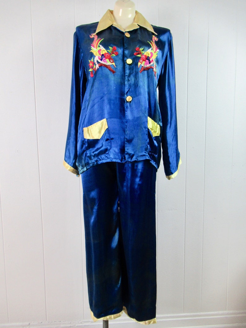 May include: A blue satin pajama set with gold trim and embroidered birds. The top has a button-up front and two pockets. The pants have a straight leg.