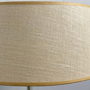 May include: A beige lampshade with a textured fabric. The lampshade has a tapered shape and is trimmed with a thin, gold-coloured band at the top and bottom. The neutral colour and simple design suggest a classic style.