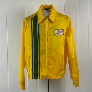 Peut inclure: Une veste en nylon jaune avec une bande de course verte sur le devant et un patch "Coca-Cola" sur la poitrine droite.