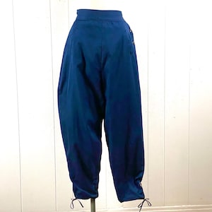 May include: A pair of dark blue, high-waisted pants with a gathered detail at the bottom of each leg. The pants have a simple design and are made of a smooth fabric.
