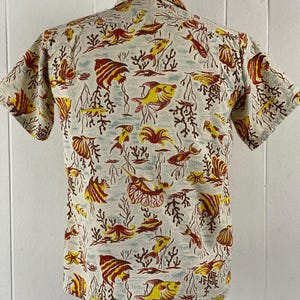 May include: A short-sleeved button-up shirt with a white background and a colorful pattern of red, yellow, and blue fish and coral.
