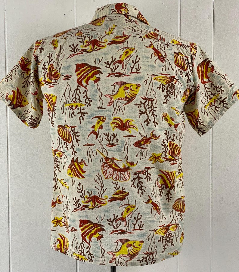 May include: A short-sleeved button-up shirt with a white background and a colorful pattern of red, yellow, and blue fish and coral.