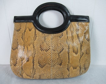 Puede incluir: Un bolso de mano de piel de serpiente de color beige con un asa superior de cuero negro y un asa redonda grande de cuero negro.