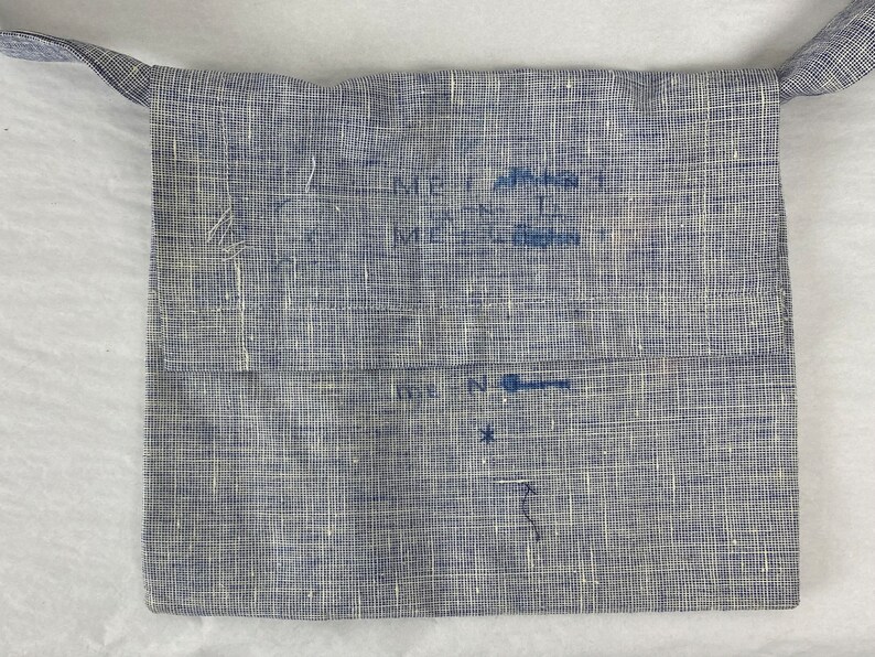 May include: A blue linen bag with a strap. The bag has handwritten text on it, including "Merrimack" and "N".