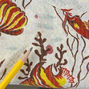 May include: A white fabric with a red, yellow, and brown fish pattern. The fabric has a few brown stains.