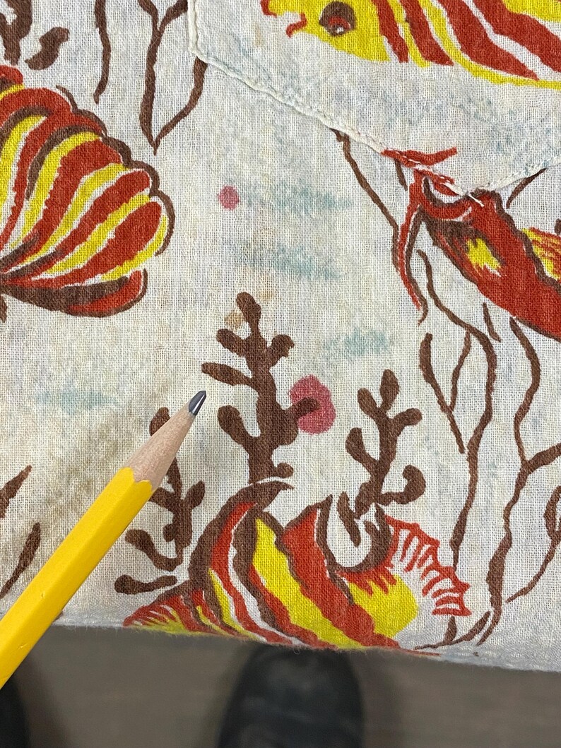 May include: A white fabric with a red, yellow, and brown fish pattern. The fabric has a few brown stains.