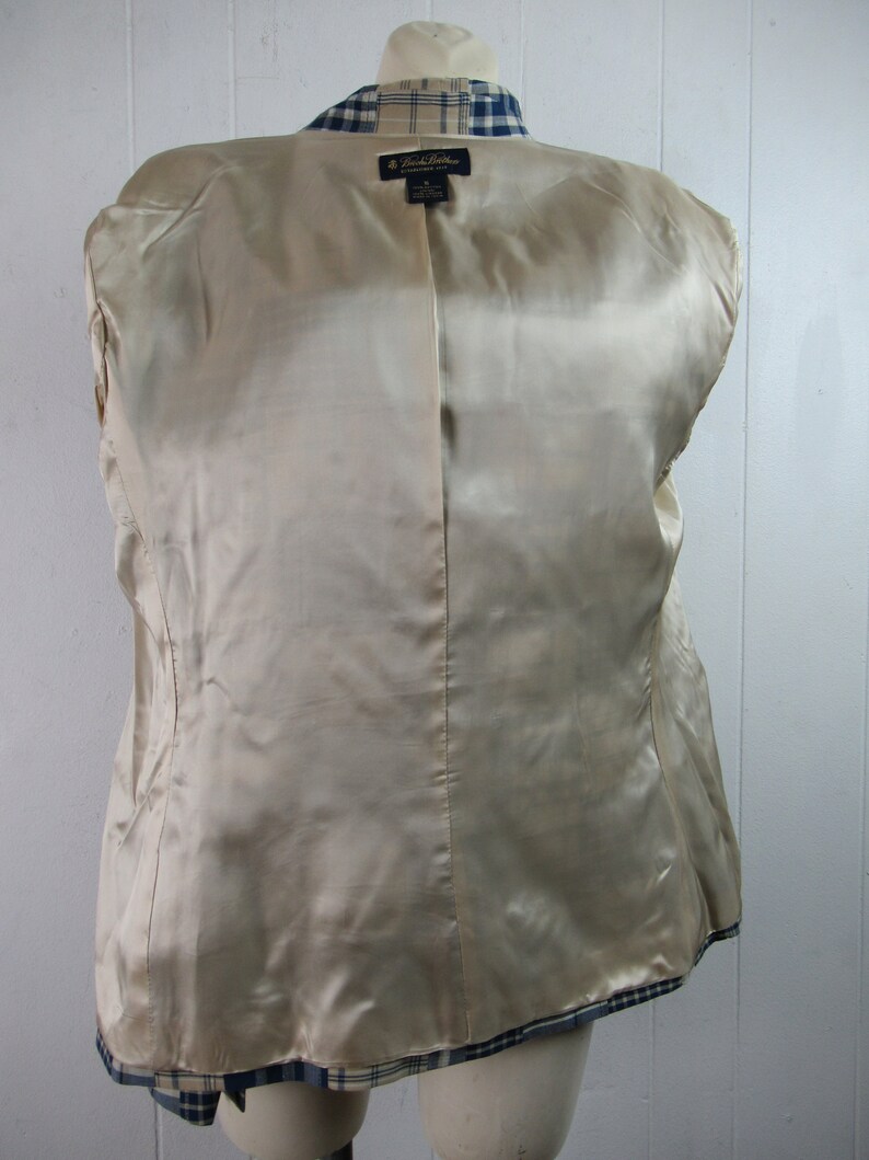 May include: A beige and blue plaid blazer with a satin lining. The blazer has a label that reads "Brooks Brothers" and "Made in Italy".