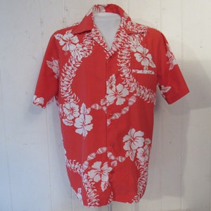 Può includere: Una camicia a maniche corte rossa con un motivo floreale bianco. Il motivo presenta fiori di ibisco e una collana di fiori.