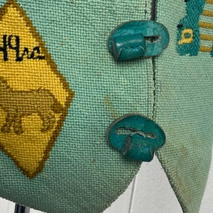 May include: A teal blue vest with a yellow and brown diamond-shaped patch with the text "49ers" embroidered on it. The vest has two teal blue buttons with a decorative design.