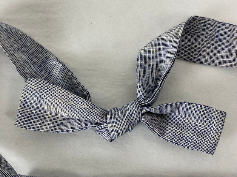 May include: A blue and white bow tie made of a textured fabric. The bow tie is tied in a knot and is ready to be worn.