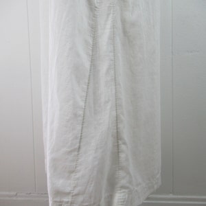 Puede incluir: Un vestido blanco de lino con un dise&ntilde;o sencillo y una falda recta. El vestido tiene una costura en el centro de la espalda y un dobladillo que es ligeramente m&aacute;s largo en la parte posterior.