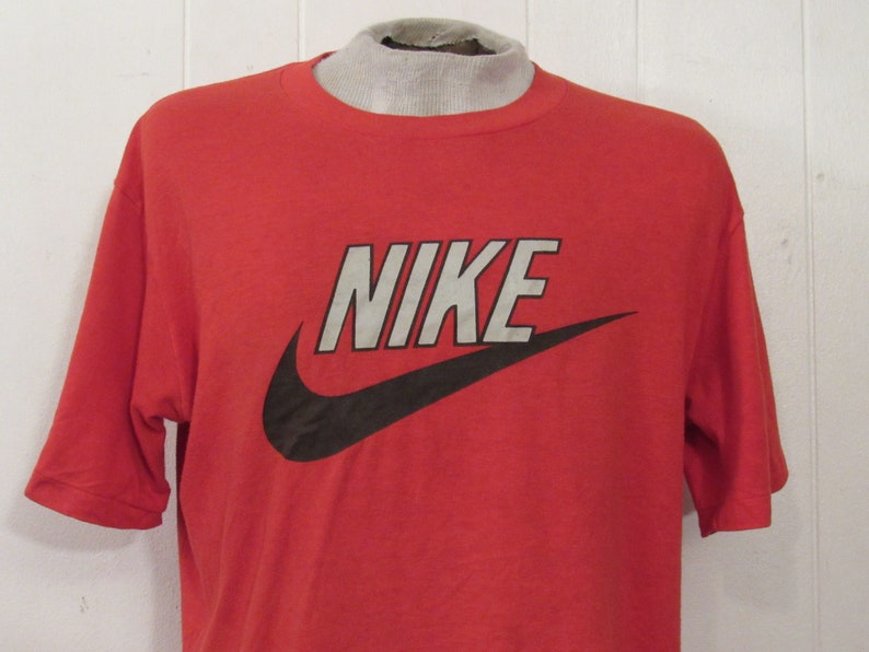 Puede incluir: Camiseta roja de manga corta con un logotipo de Nike en blanco y negro. El logotipo es un swoosh con la palabra "NIKE" en letras blancas.
