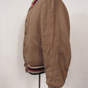May include: A brown bomber jacket with a ribbed collar and cuffs. The cuffs have red, white, and blue stripes.