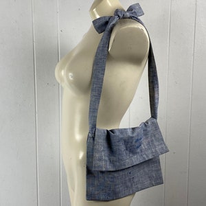May include: A blue linen crossbody bag with a long strap. The strap is tied in a bow at the top of the bag.