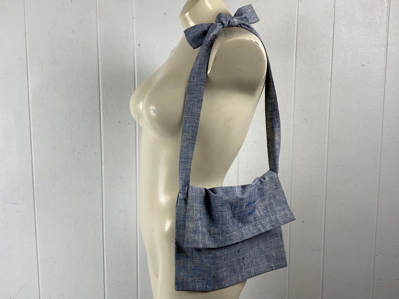 May include: A blue linen crossbody bag with a long strap. The strap is tied in a bow at the top of the bag.