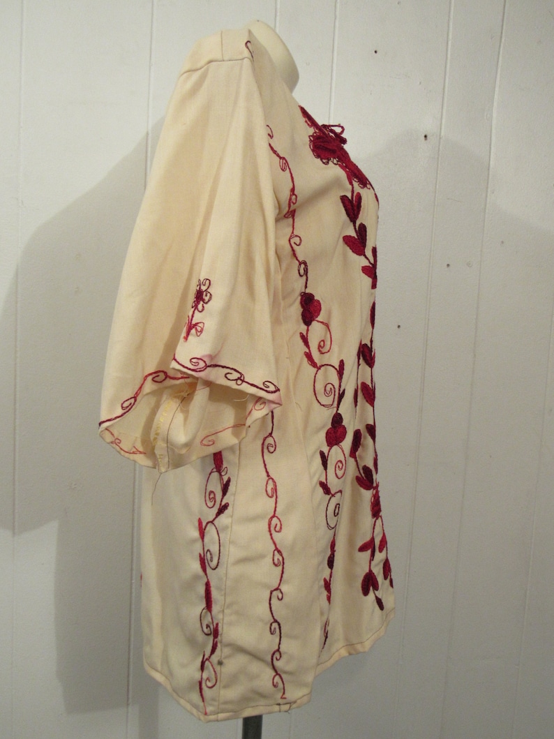 May include: A white tunic with red embroidered floral designs. The tunic has a loose fit and a round neckline.