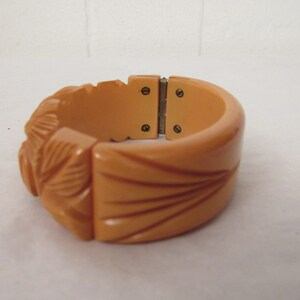 Puede incluir: Un brazalete vintage de baquelita de color melocot&oacute;n, tallado, con cierre de bisagra.
