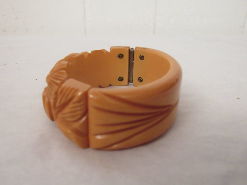 Puede incluir: Un brazalete vintage de baquelita de color melocot&oacute;n, tallado, con cierre de bisagra.