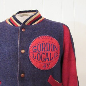 May include: A navy blue and red varsity jacket with a red patch on the left side that says "Gordon Local 12 47".