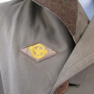 May include: A brown jacket with a brown corduroy collar and a gold eagle patch on the left side of the chest.