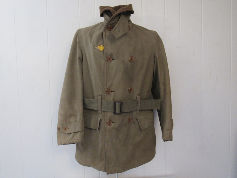 May include: A brown double-breasted jacket with a belt and a yellow patch on the left side of the chest.
